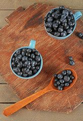 Fresh blueberries in cups and spoon on wooden table close up