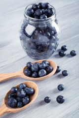 Fresh blueberries in spoons and jar on wooden table close up