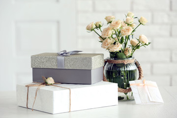 Obraz premium Beautiful gift boxes with bouquet of flowers on the table in front of brick wall, close up