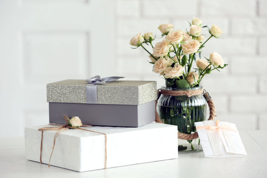 Fototapeta Beautiful gift boxes with bouquet of flowers on the table in front of brick wall, close up