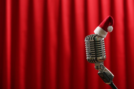 Vintage microphone with little Christmas hat on red curtain background