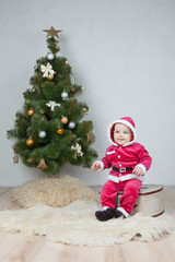 Small boy in Santa suit plays near new-year tree in white studio