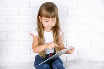 Little girl with tablet on brick wall background