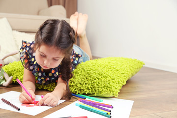 Cute little girl  sitting on floor and drawing picture, on home interior background