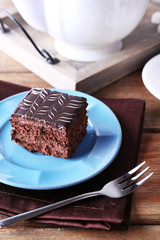 Sweet chocolate cake on blue plate with cup of tea on brown cotton serviette, close up