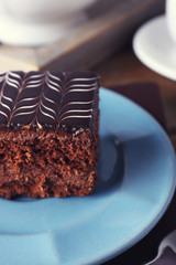 Sweet chocolate cake on blue plate with cup of tea on brown cotton serviette, close up