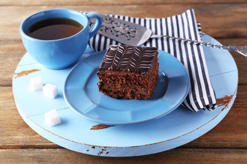Sweet chocolate cake on blue plate with cup of tea on wooden table