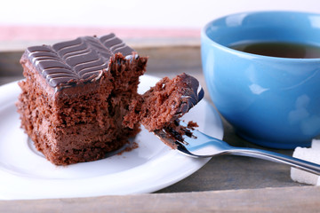 Served table with a cup of tea and chocolate cake on wooden background close-up
