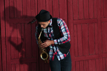 Young man playing on saxophone outside near the old wall