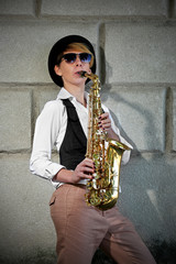 Attractive woman in hat plays saxophone on brick wall background