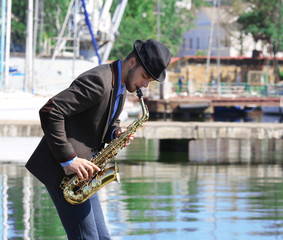Young handsome man plays saxophone on river park background