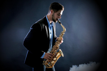 Fototapeta na wymiar Elegant saxophonist plays jazz on dark background in a smoke