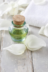 Obraz na płótnie Canvas Bottle of green essential oil, white rose petals and soft towel