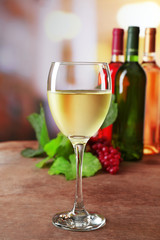 White wine glass with colourful bottles on wooden table against unfocused background