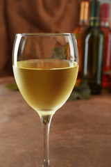 White wine glass against different bottles and grape on wooden table