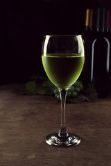 White wine glass against different bottles and grape on wooden table