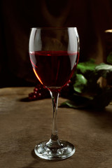 Red wine glass against wicker basket with grape and wine bottle on wooden table