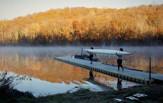 Crew team carries row boat out to the lake during sunrise