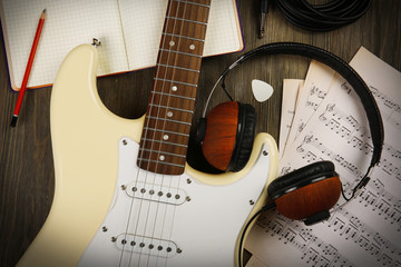 Electric guitar with headphones, musical notes and note book on wooden background