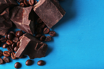 Black chocolate pieces and coffee grains on color wooden background