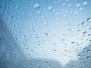 Raindrops on car's glass with blurry cloudy sky.