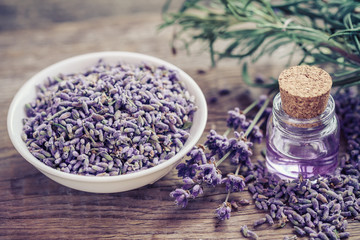 Bottle of essential oil and lavender flowers in bowl and on tabl