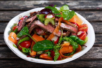 Spicy Beef Meat Salad with Carrots, Tomatoes, Cucumber, Parsley and Salad leaves Spinach, rocket, red ruby chard on old wooden table.