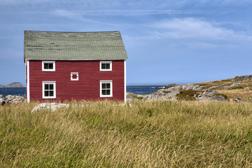 Obraz premium Tilting / Abandoned house with a disintegrating dory in front of it sits on the coastline in the town of Tilting on Fogo Island, Newfoundland and Labrador