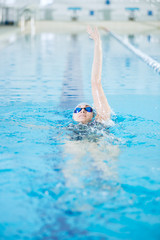 Young girl in goggles swimming back crawl stroke style