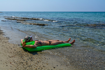 Beautiful young woman sunbathing on a stone beach on an air matt