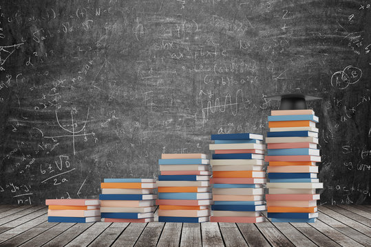 A stair is made of colourful books. A graduation hat is on the final step. Black chalk board with math formulas on the background. Wooden floor.