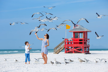 Young mother and her son feeding seagulls on tropical beach - 94881069