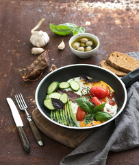 Pan of fried eggs, salami, asparagus, cherry-tomatoes with bread, fresh basil, olives and garlic on grunge rusty table surface