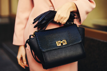 Elegant outfit. Closeup of black leather bag handbag in hand of stylish woman. Fashionable girl on...