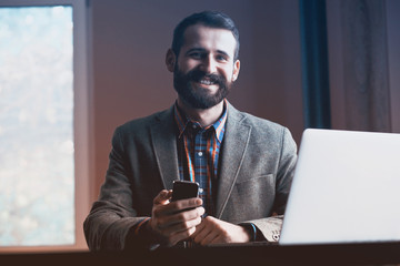 smiling bearded man working with laptop and phone
