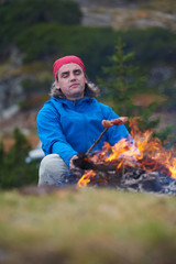 hiking man prepare tasty sausages on campfire