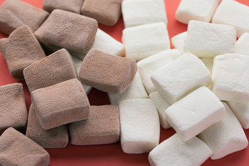 Pile of chocolate and original flavours of marshmellows in red pastel background