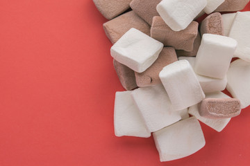 Pile of chocolate and original flavours of marshmellows in red pastel background - close-up