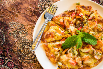 Seafood and sausage pizza on white dish and flower textile backg