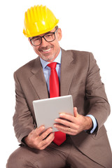 smiling old construction engineer holding a tablet pad and sitti
