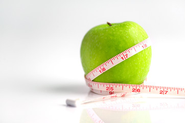 Measuring tape wrapped around a green apple as a symbol of diet