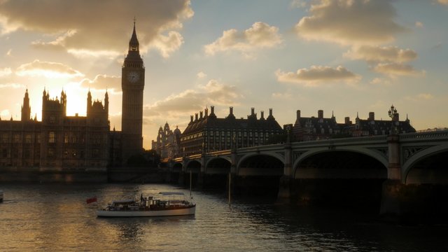 River boat passes under Westminster Bridge at the moment the sun sets behind the Houses of Parliament. Shot in 4K