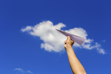 Holding paper airplane before throwing with blue sky background.