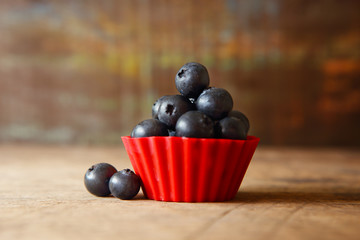 Closeup Fresh Blueberries in Red Cup on Wooden Background.