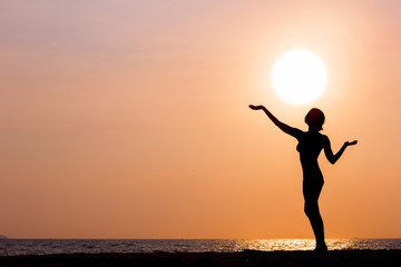 Fototapeta premium Female silhouette standing on sunset sea background, back lit