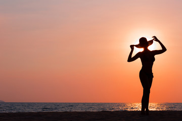 Woman silhouette with hat standing on sunset sea background, back lit