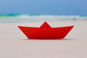 Red paper boat on white sand seashore, blue sea background