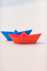 Red and blue paper boats on white sand seashore