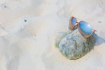 Fototapeta na wymiar Sunglasses lying on a stone on the beach, white sand