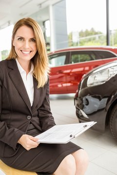 Smiling saleswoman sitting near cars